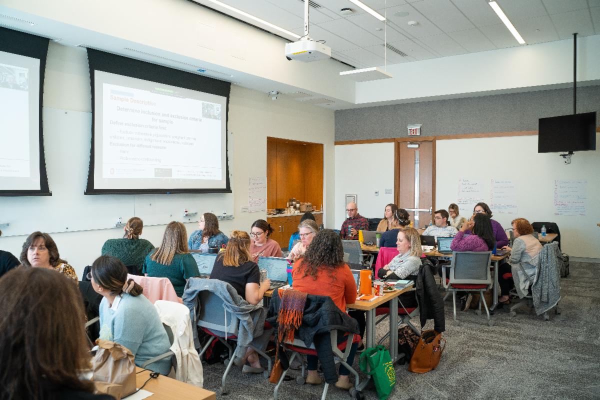 Group of participants gathered at tables and watching projected information on the screen