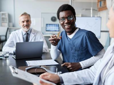 happy young nurse in uniform conversing with mature female colleague sitting next to him