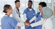 A group of doctors and nurses in blue scrubs putting their hands together to show teamwork.