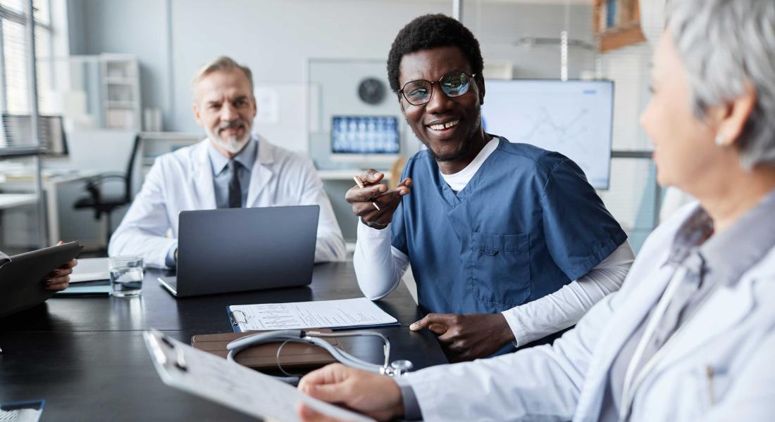 happy young nurse in uniform conversing with mature female colleague sitting next to him